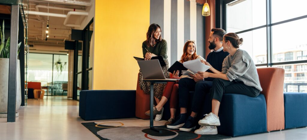 Multicultural businesspeople working in an office lobby. Group of happy businesspeople smiling while sitting together in a co-working space. Young entrepreneurs collaborating on a new project.