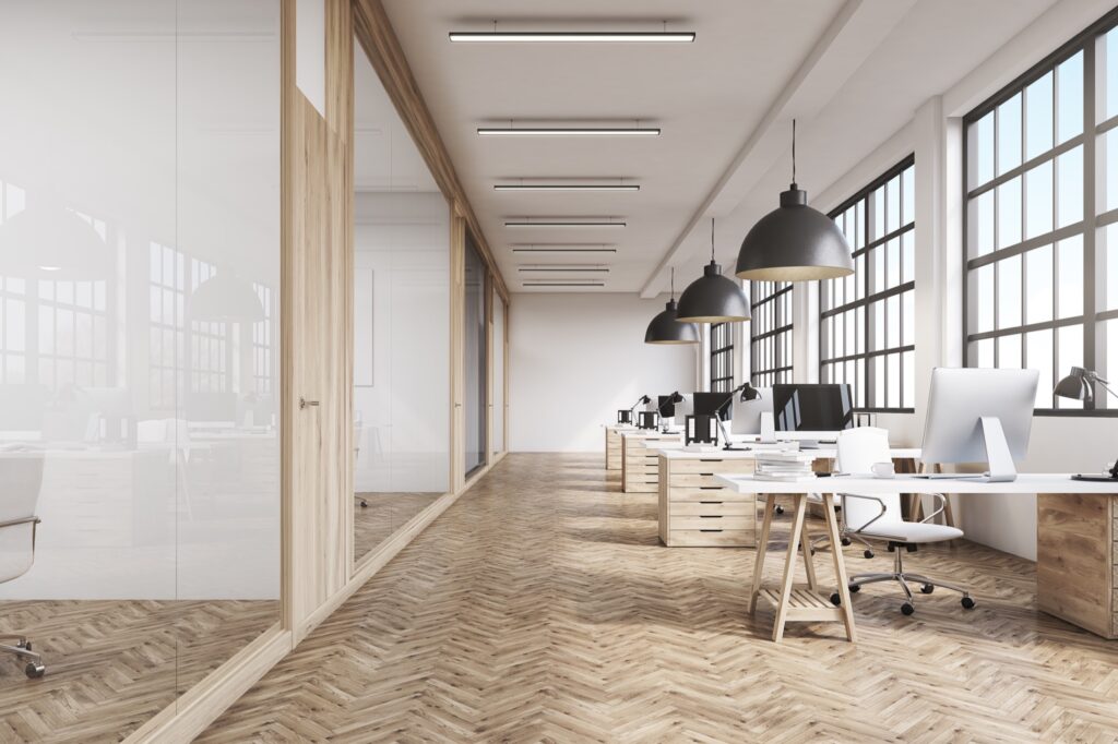 Front view of an office interior with a row of dark wood tables standing under large windows. Massive ceiling lamps. Computers. 3d rendering.